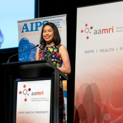 a woman stands at a lectern with banners behind her